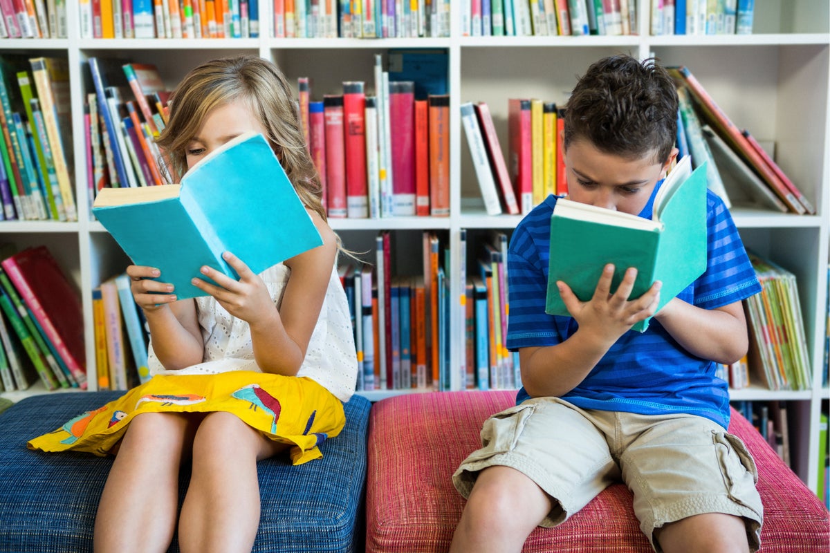 Two children read books in a library.