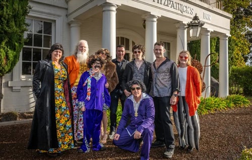 Group of people dressed in costumes stand in front of an old pub.