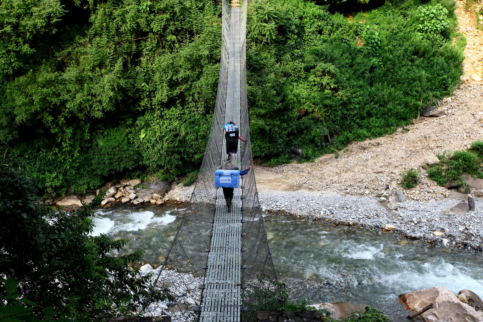 Health workers deliver vaccine over a bridge. 