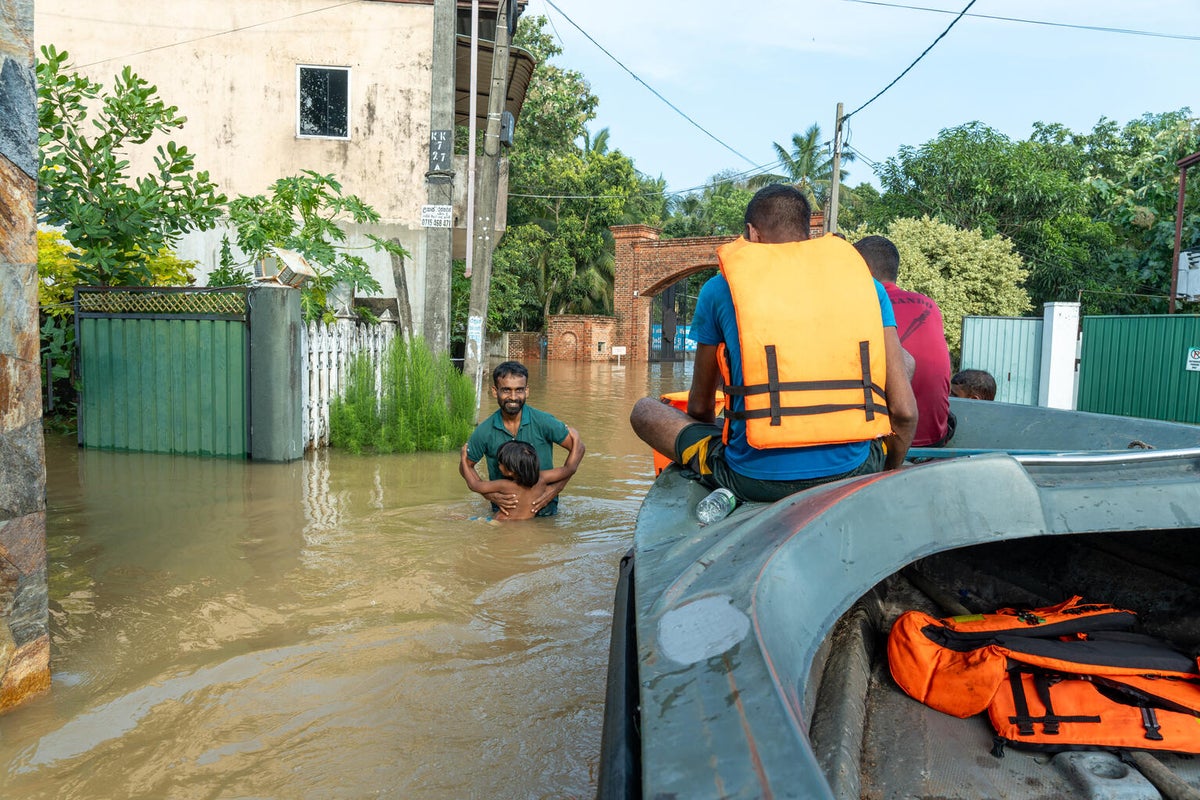 Father and child wade through flood waters as a boat passes