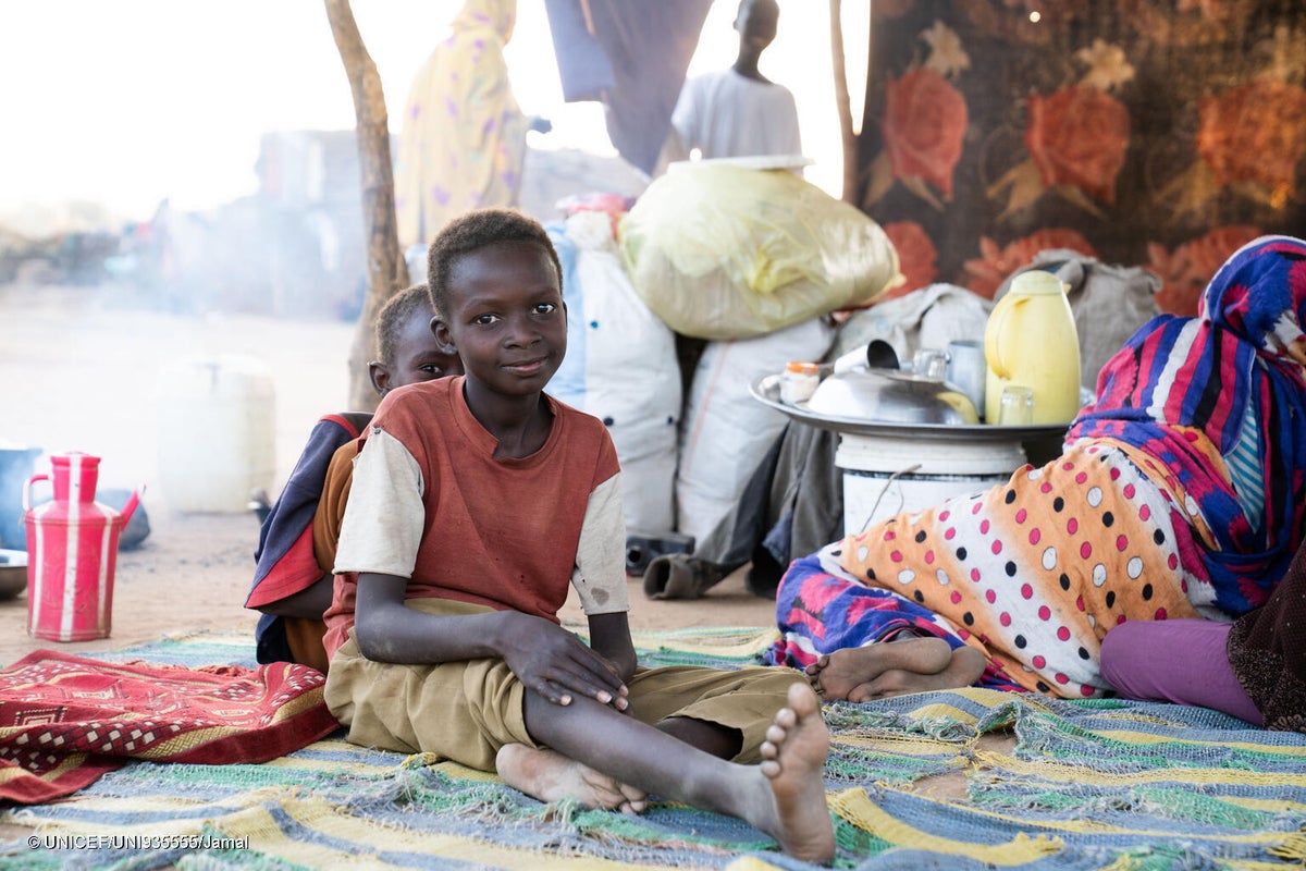 Two children sitting on the ground inside a tent.