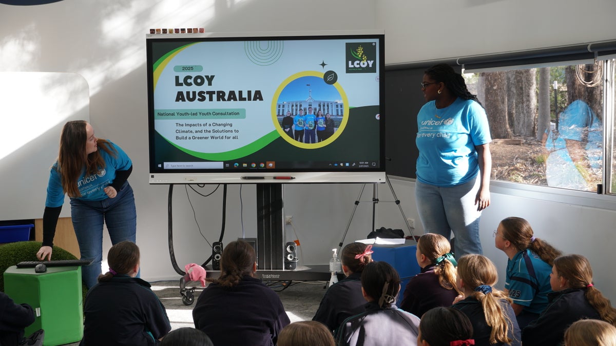 UNICEF Australia Young Ambassador Princess and a UNICEF Australia staff member stand in front of a group of primary school children, presenting to them during an LCOY event. 