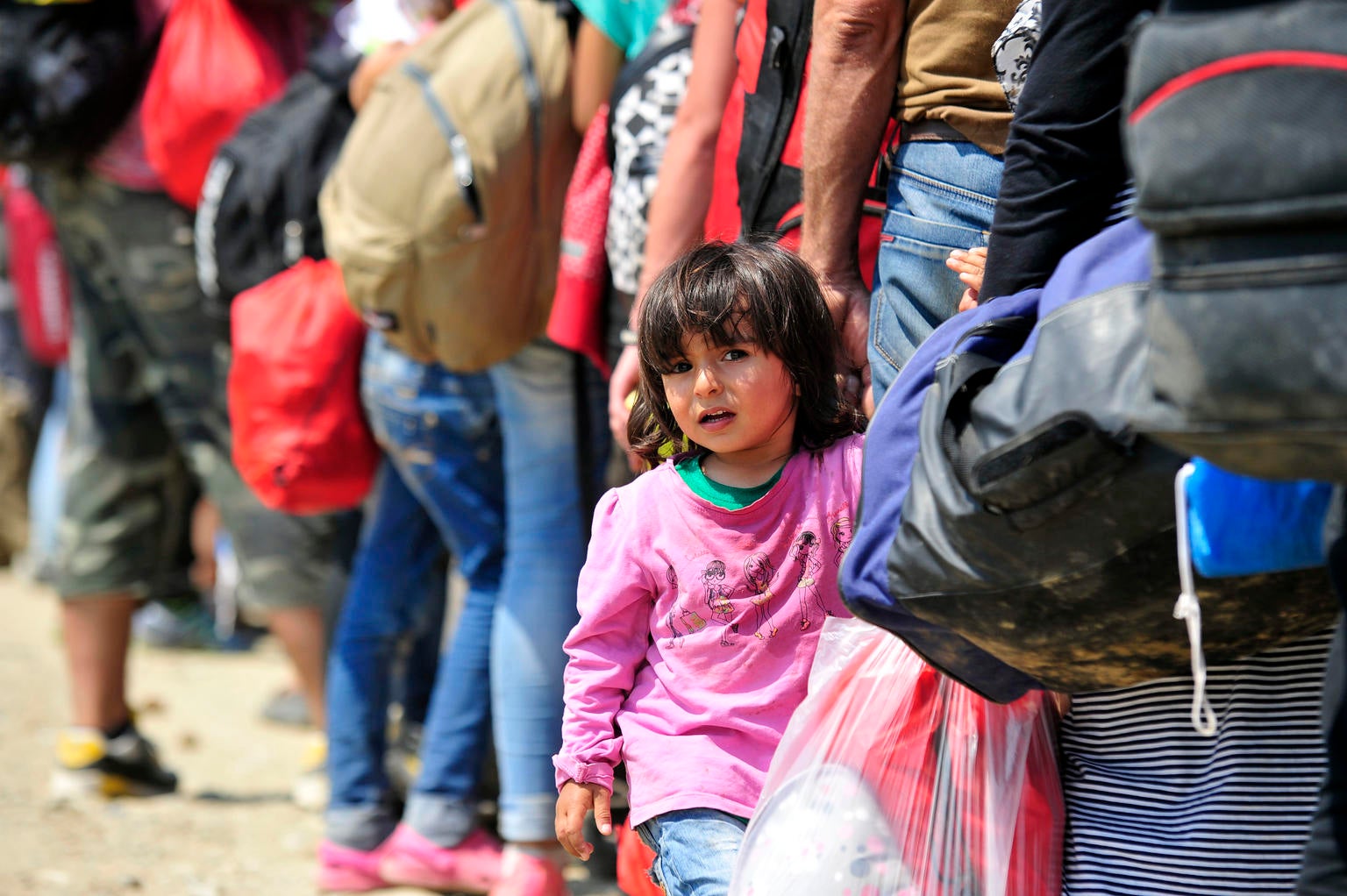  a young girl from the Syrian Arab Republic holds the hand of an adult while standing in a queue of people waiting to board a train to the border with Serbia