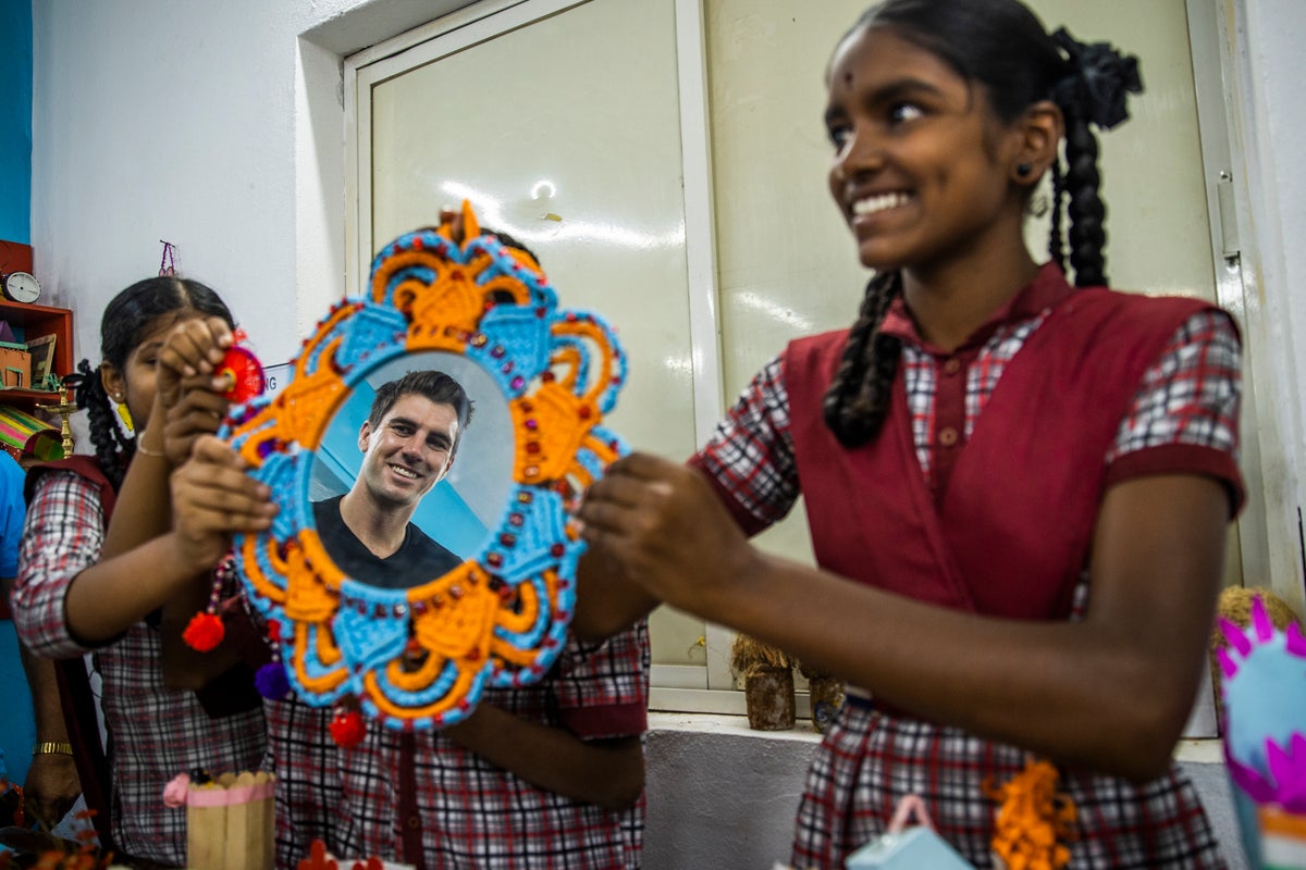 Two young students hold up a mirror to Pat Cummins' face. 