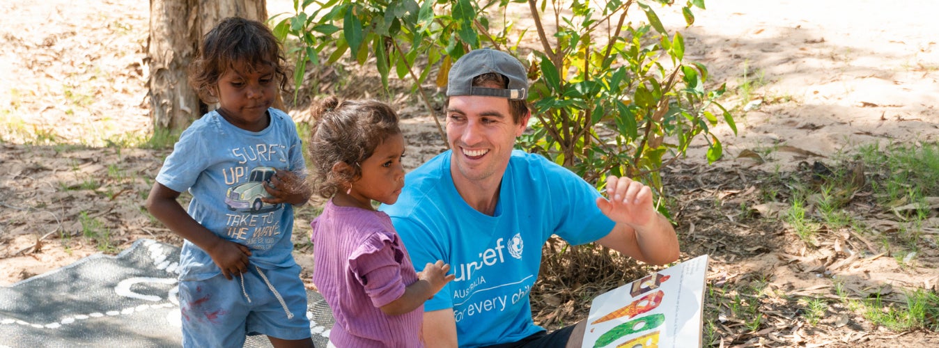 A young man reads a book to two children. 