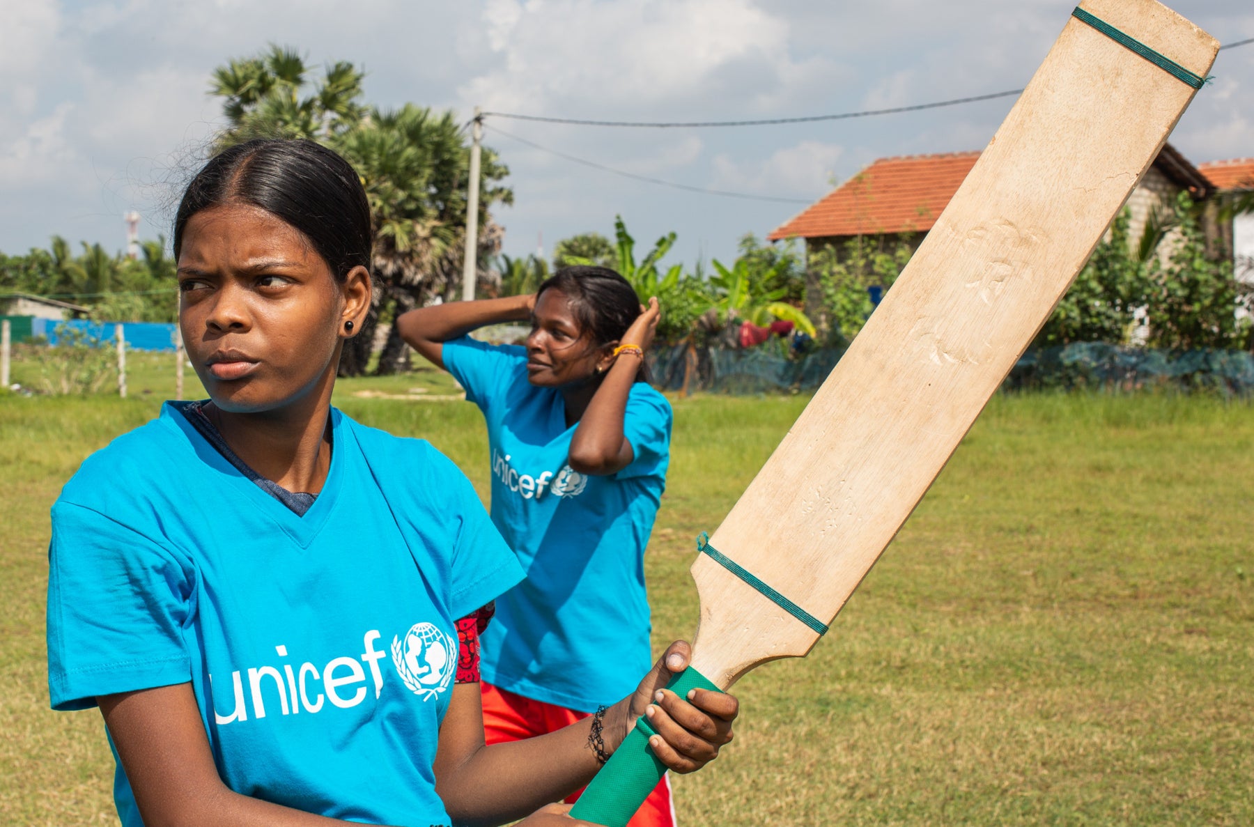 A young woman holds a cricket bat and is waiting for the bowl.