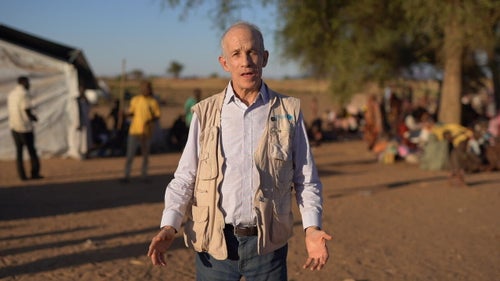 Man in front of tent and tree with people in background