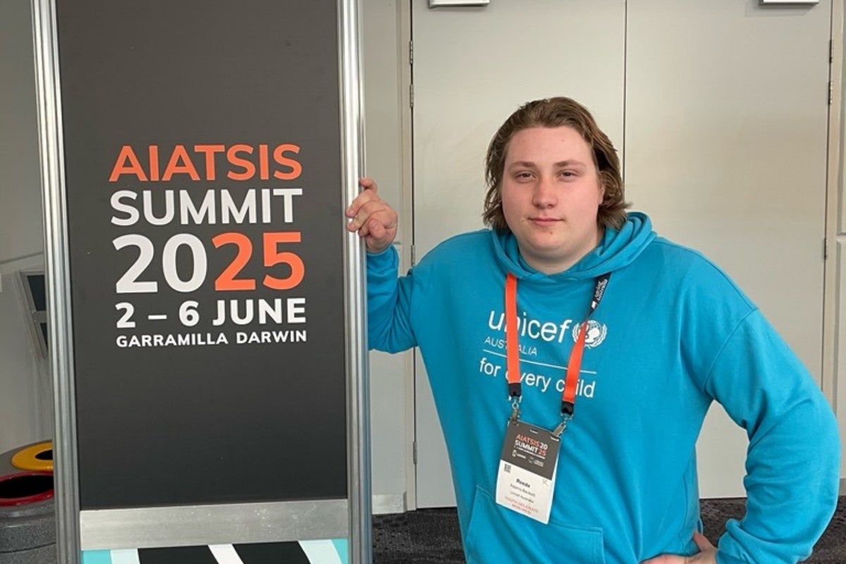 Young Ambassador Reede stands next to a sign for the 2025 AIATSIS Summit.