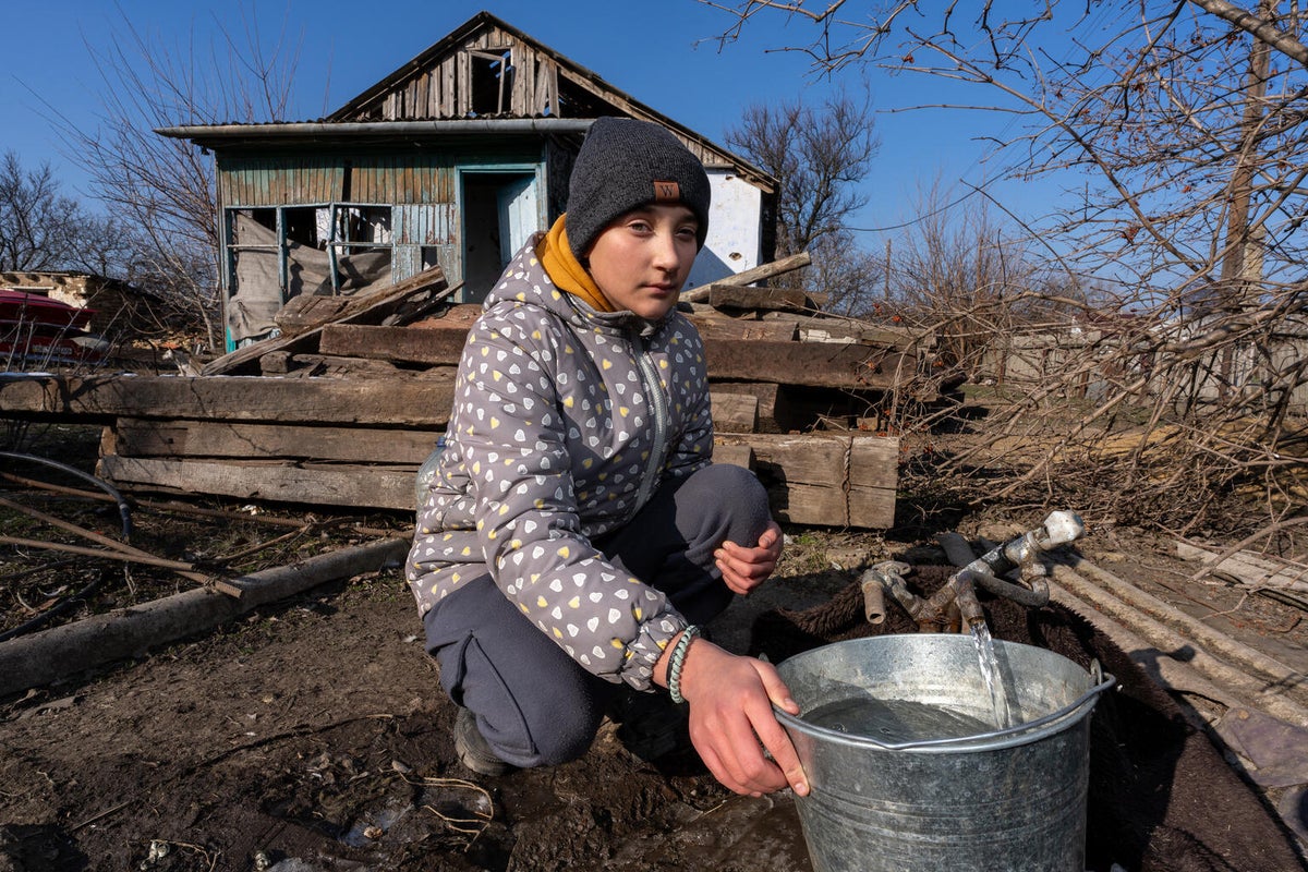 14-year-old Yana draws water from a well near her destroyed home. 