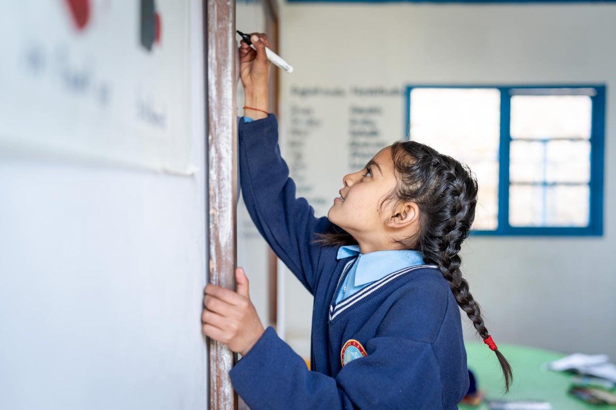 A young girl writes on a whiteboard. 