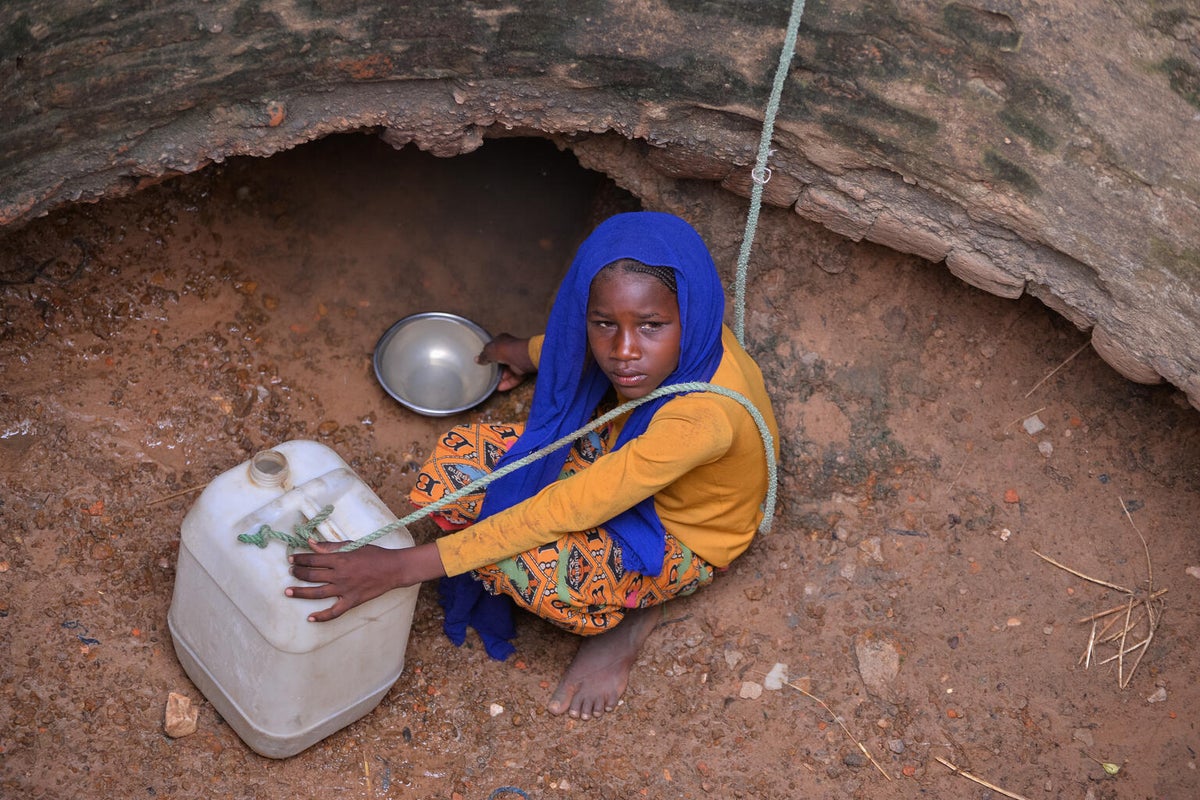 Muzdalifa, 12-years-old, scoops water from a spring at the bottom of a deep well using a metal container to fill a 20 litre jerrycan.