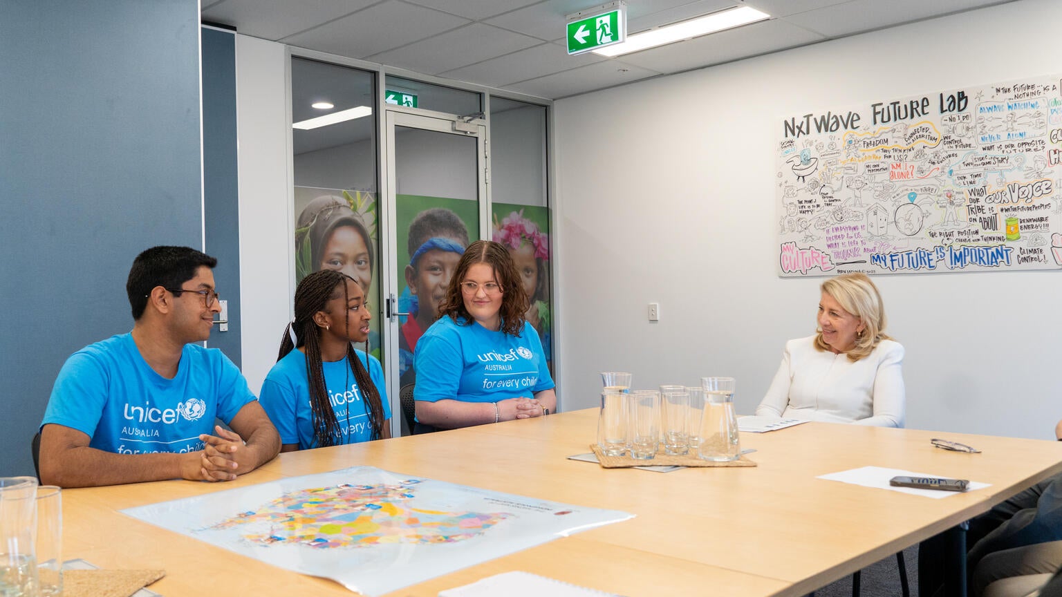 A woman in a white top sits in a room listening to three young adults in blue tops. 