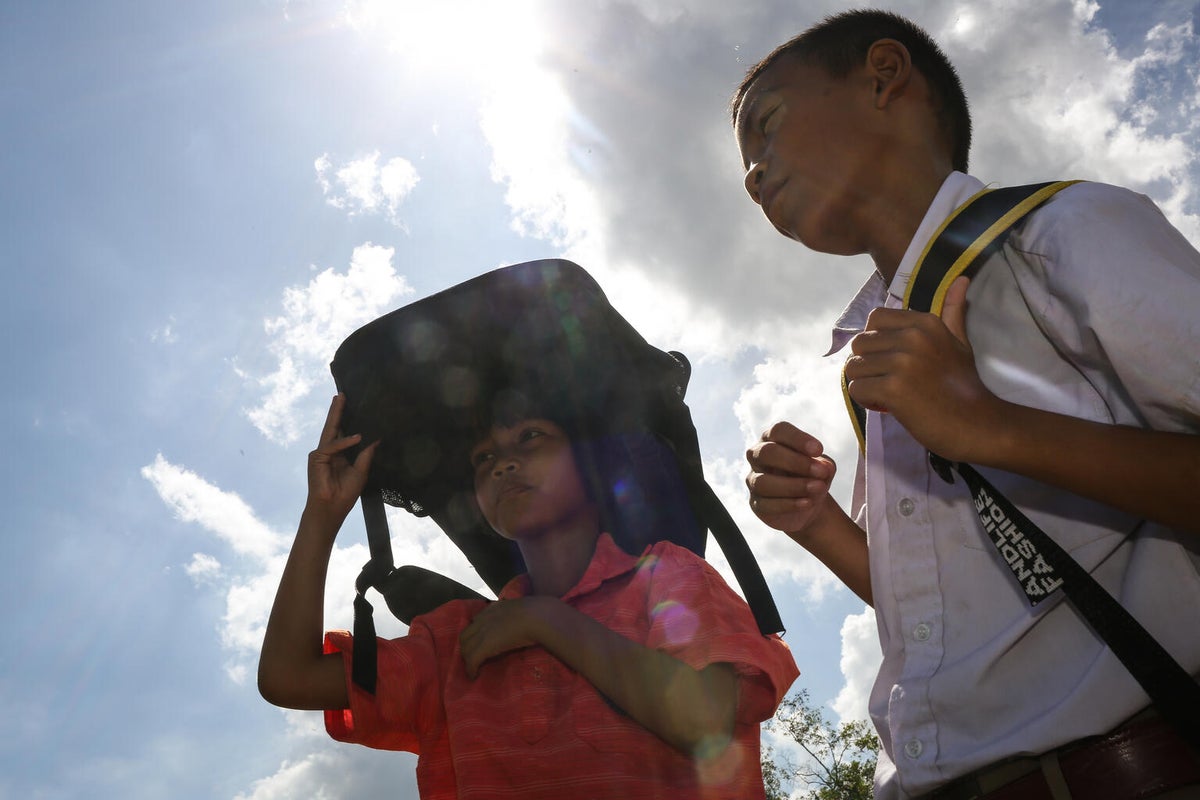 Karaked, a 10-year-old fourth-grade student, and Pattawee shield themselves from the heat as they walk back to the classroom after an afternoon break.