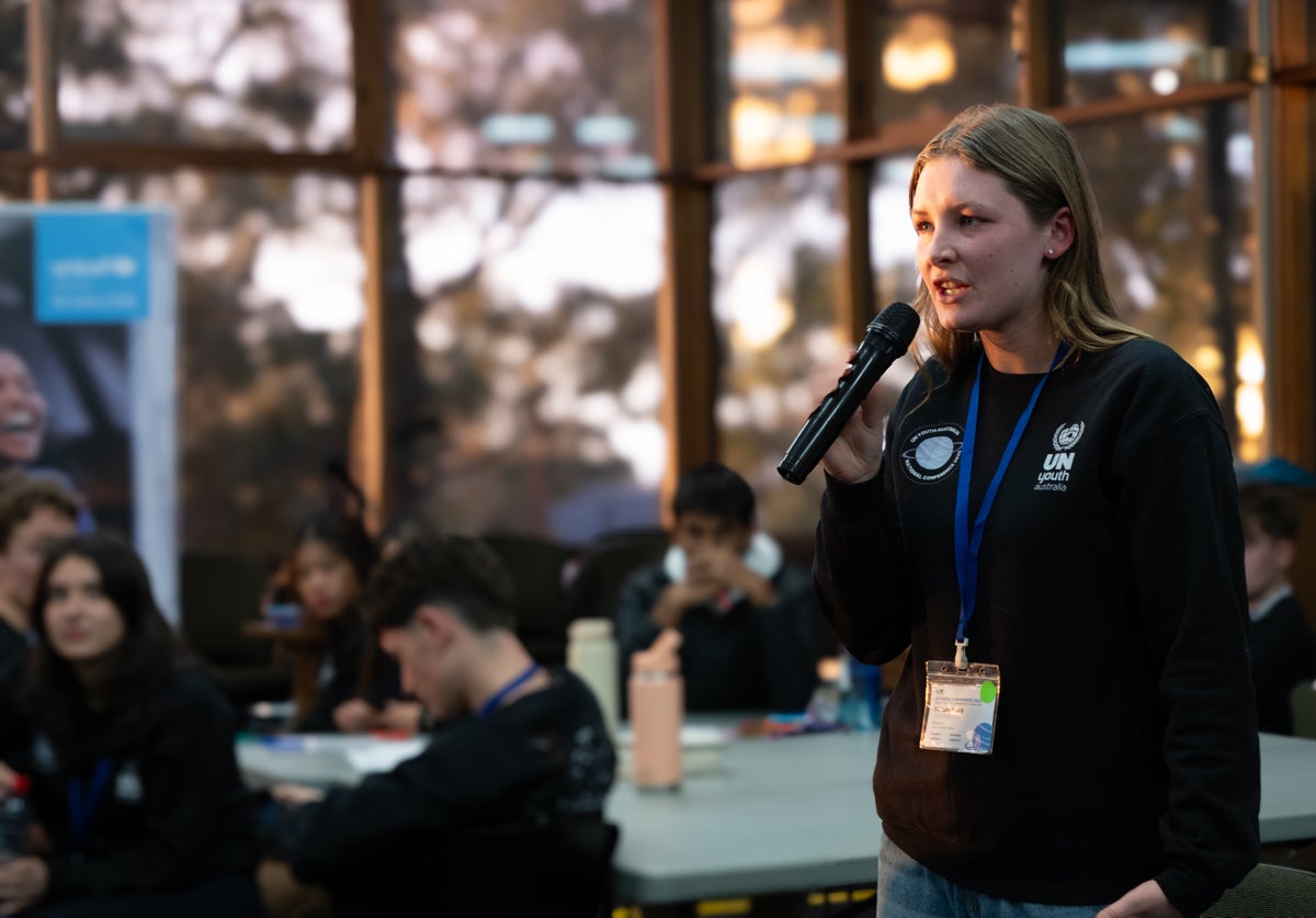 A young woman holding a microphone stands as she addresses a room of people during an LCOY in Adelaide. 