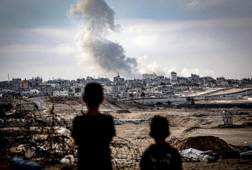 Two children standing and looking at smoke rising over Gaza.