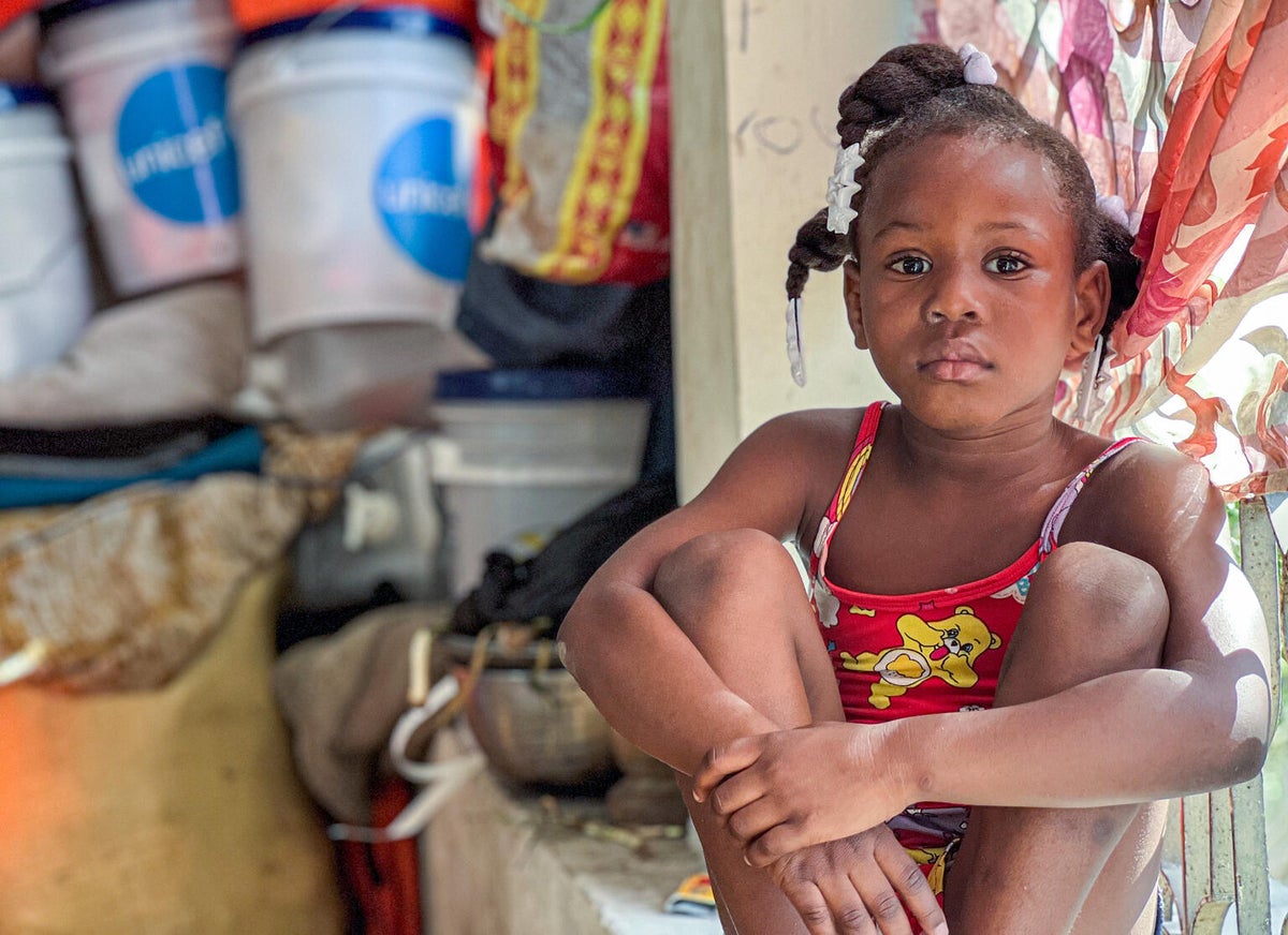 Lovely, 9, sits quietly inside a crowded public space that has serves as her family’s shelter since they fled armed group violence in Haiti.