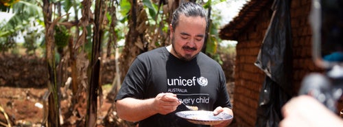 A man preparing a meal on an outdoor table with a group of people watching him.