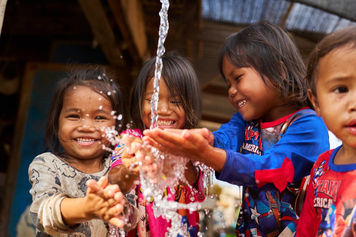 Three children wash their hands using piped water in Cambodia. 