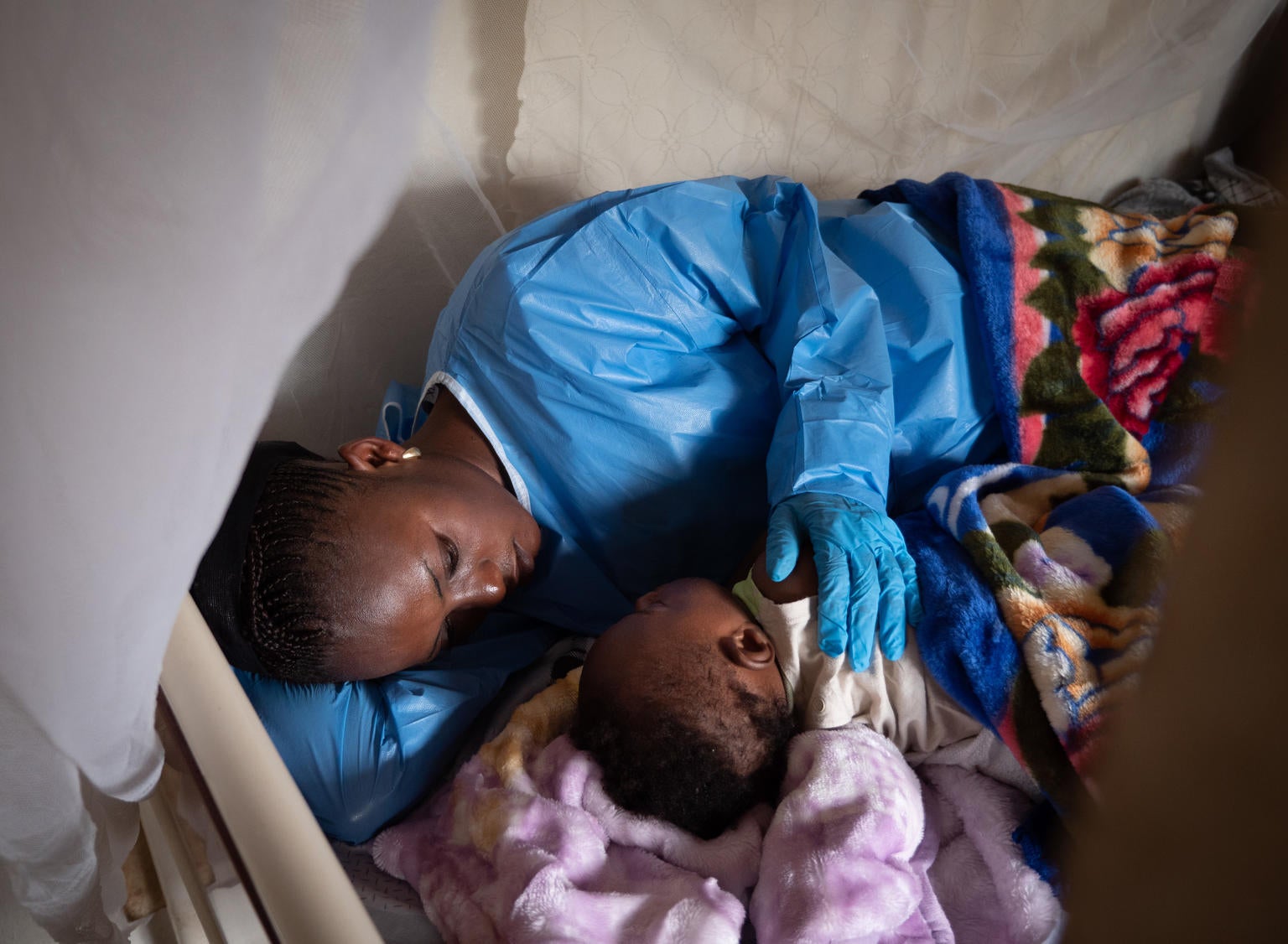 A woman with a protective gown and gloves as lying next to a baby.