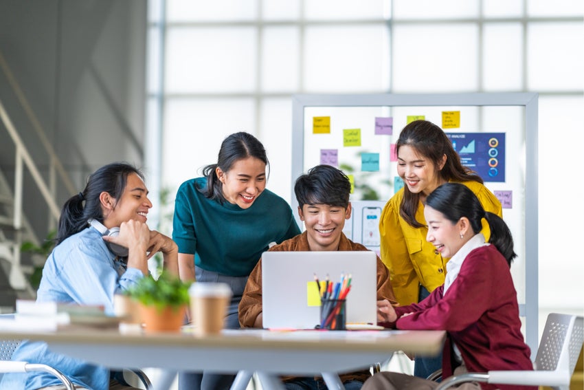 A group of young people gather around a laptop.