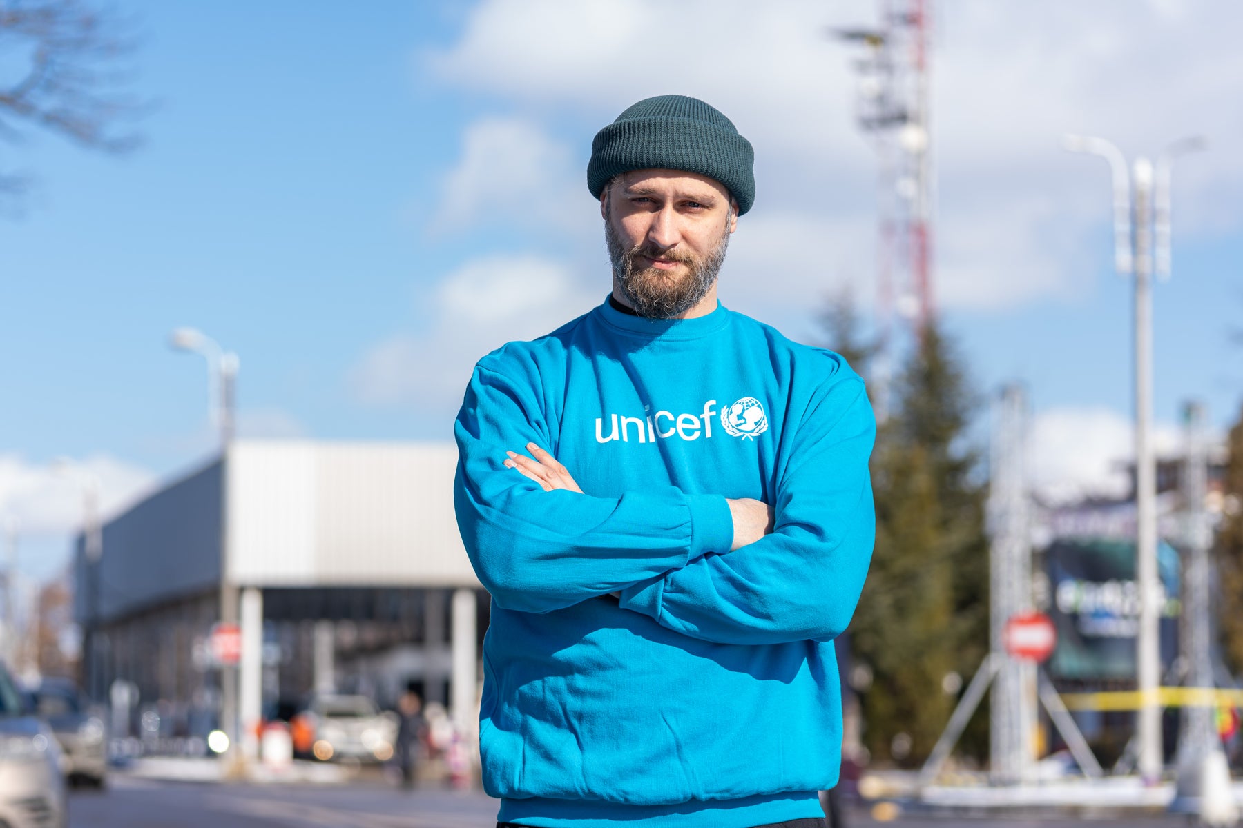 UNICEF worker looks at camera. Wearing blue shirt and beanie.
