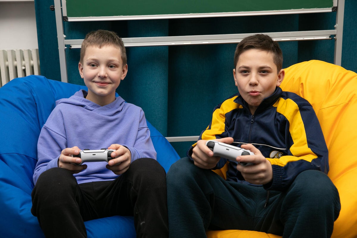 Two young boys sitting on beanbags and holding controllers play a video game together.  