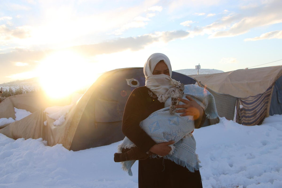 A mother carrying her child in front a tent. 