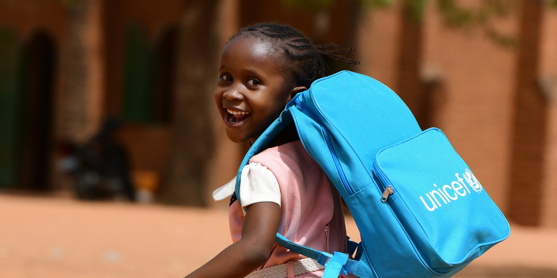 A girl wearing a UNICEF backpack and school uniform runs in a playground in Niger. 