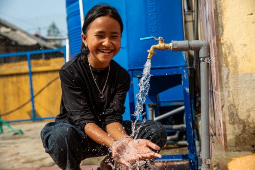 A girl child can be seen smiling and washing her hands from a tap