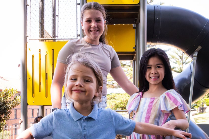 A group of three children smile as they pose on a playground.