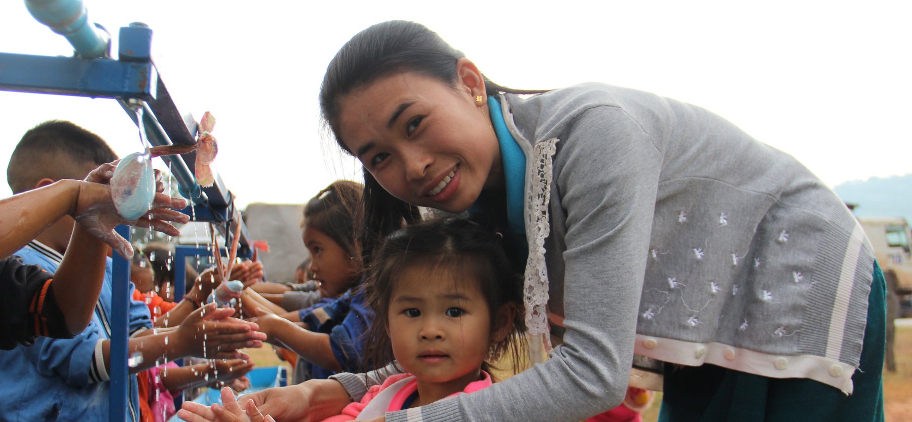 A woman is helping a young girl wash her hands in and outdoor washing facility.