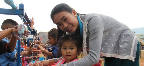 A woman is helping a young girl wash her hands in and outdoor washing facility.
