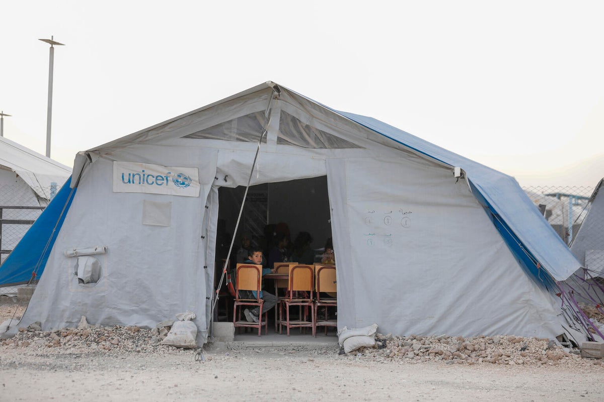 A boy sits instead a classroom in a tent. 