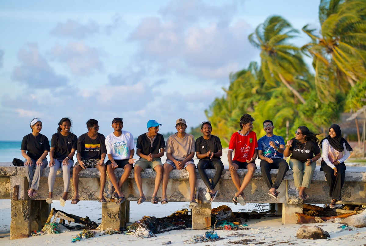 A group of young people sit on a sea wall in the Maldives.