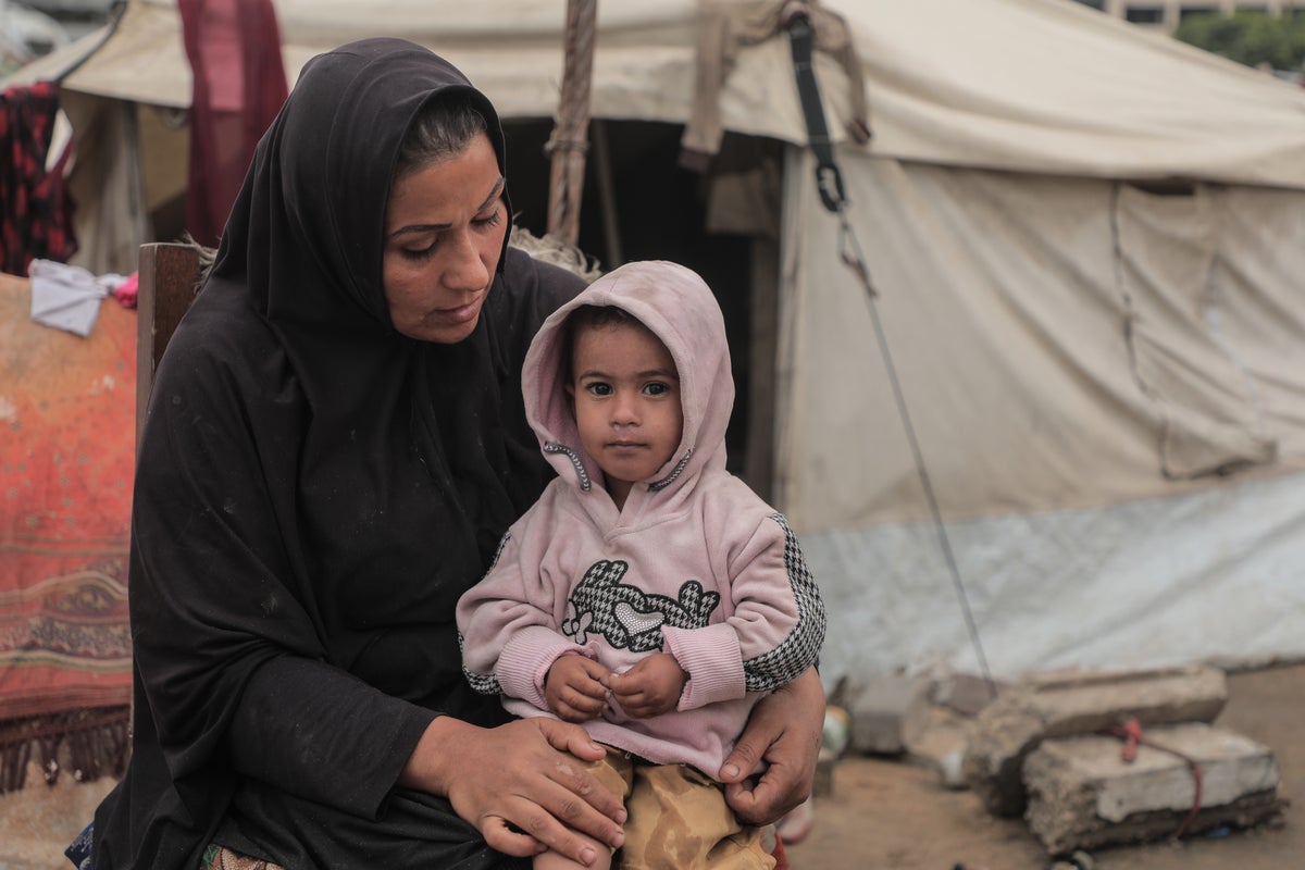 A woman holds her young child in front of the tent where they live in Gaza. 
