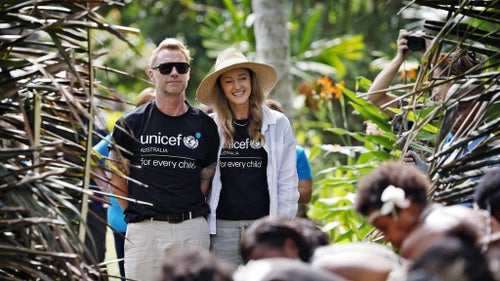 Man and woman in UNICEF t-shirts walk through a PNG village.
