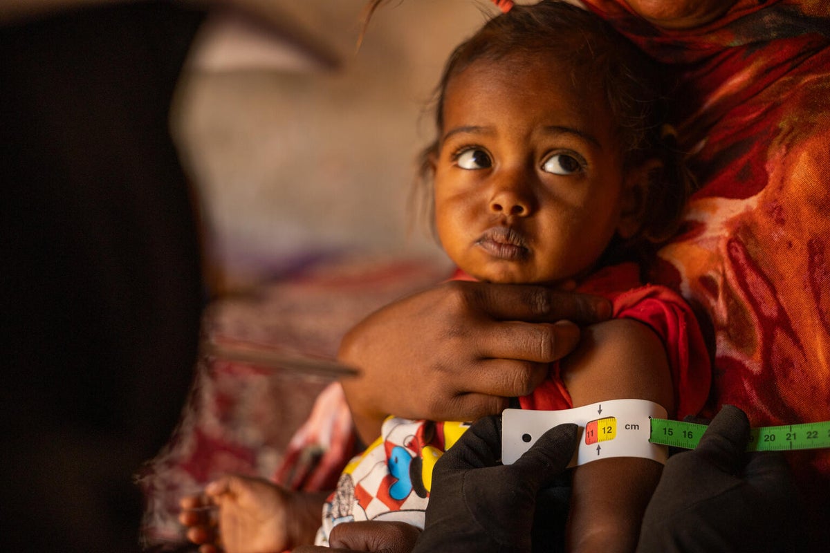 Child held in the arms of an adult with a tape measure around their upper arm