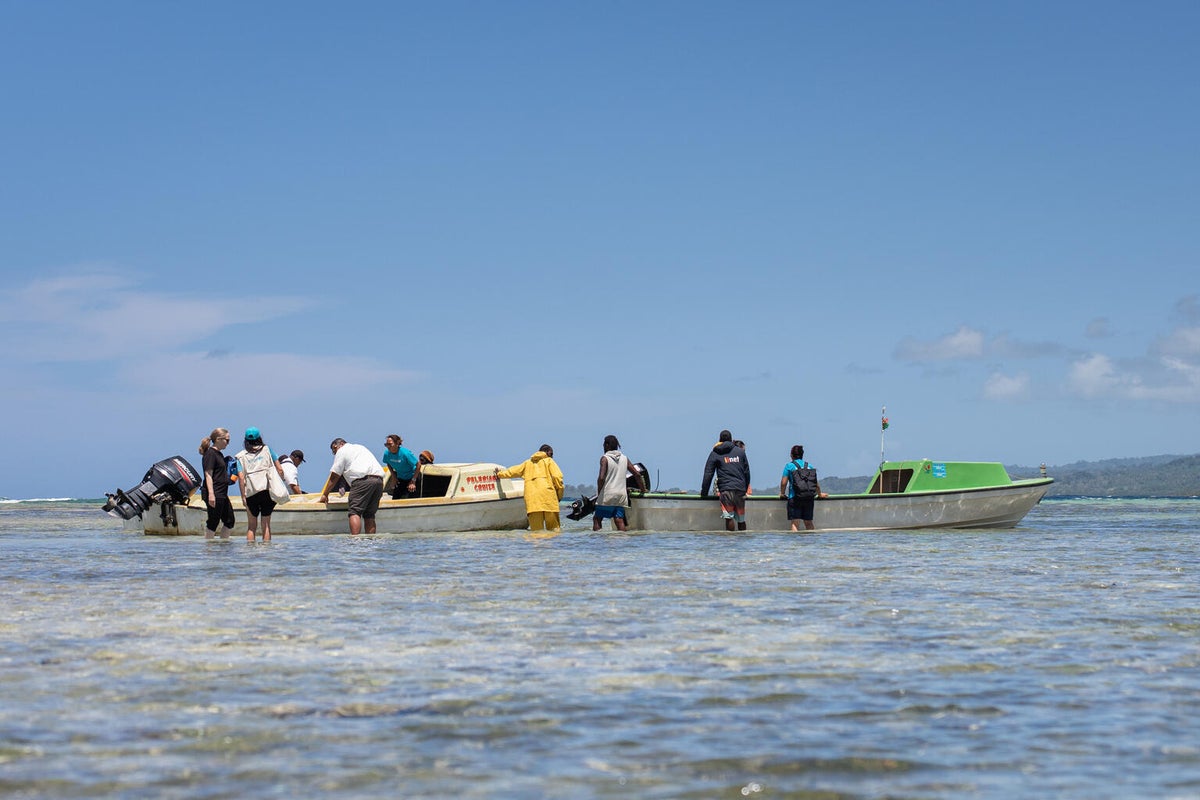 A group of people waking towards two small boats on a beach