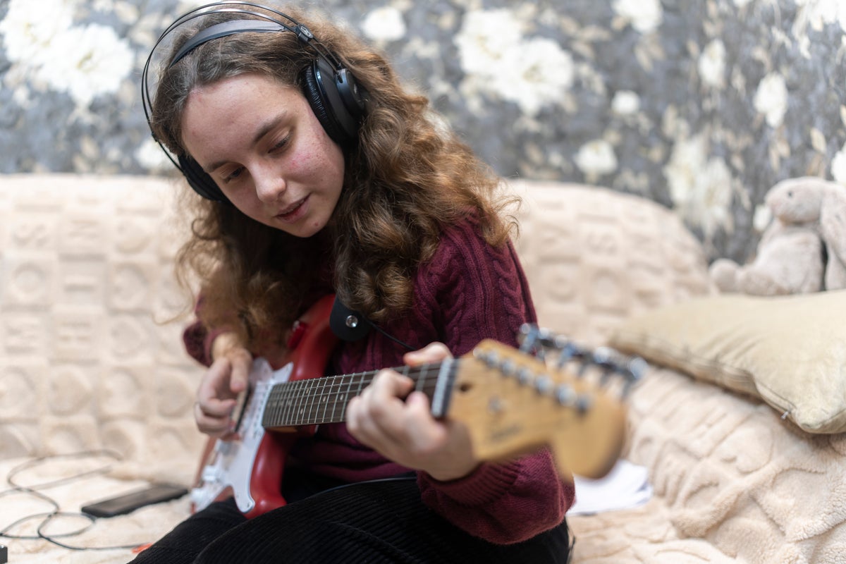 16-year-old Veronika from Ukraine plays her electric guitar while sitting on a couch in her house.