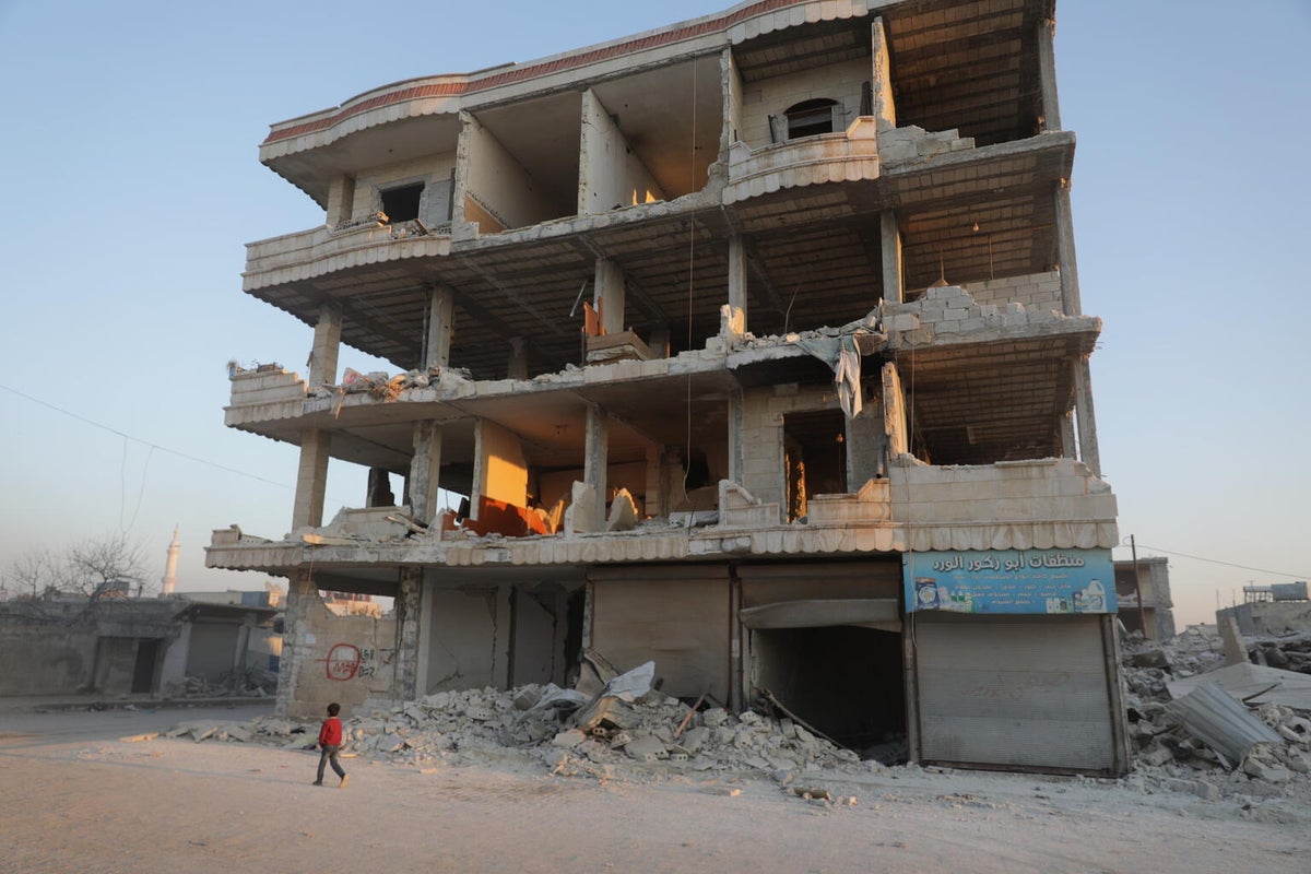 A child walks in front of a dilapidated building.  