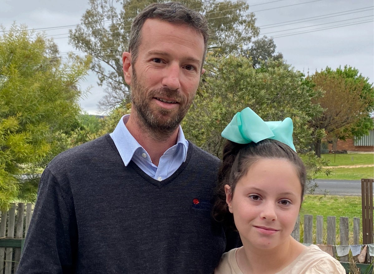 A man wearing a blue collared shirt poses with his young daughter. 