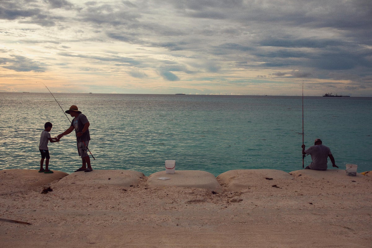 Tuvaluan locals fish standing on sandbags positioned around the perimeter of ‘The Reclaimed Land’.
