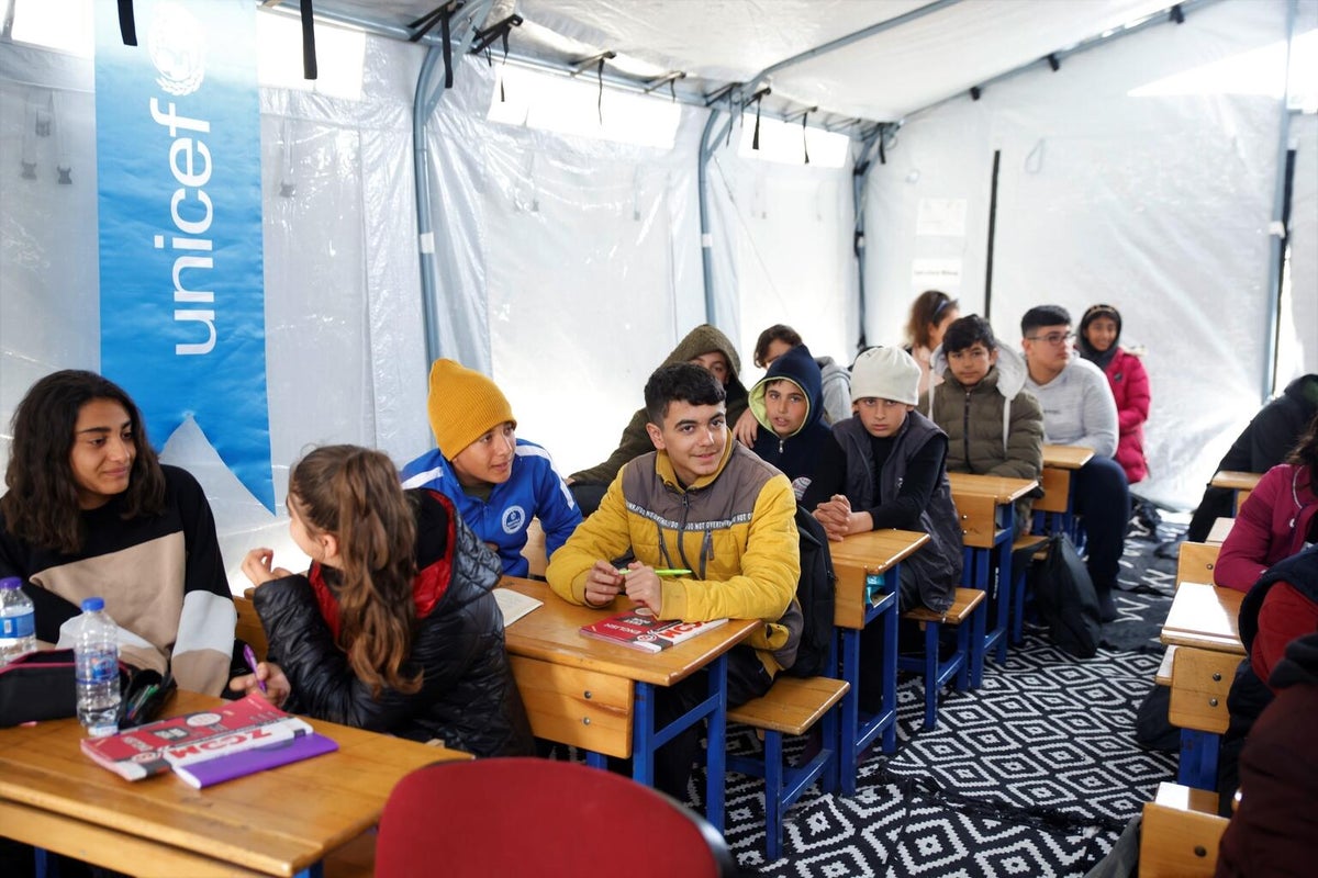 A group of school children attend a lesson in a tent classroom with UNICEF branding
