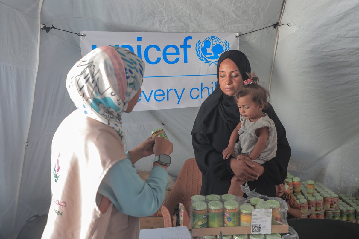 A mother holds her 1-year-old child as a health worker gives them a tin of therapeutic milk in a UNICEF tent. 