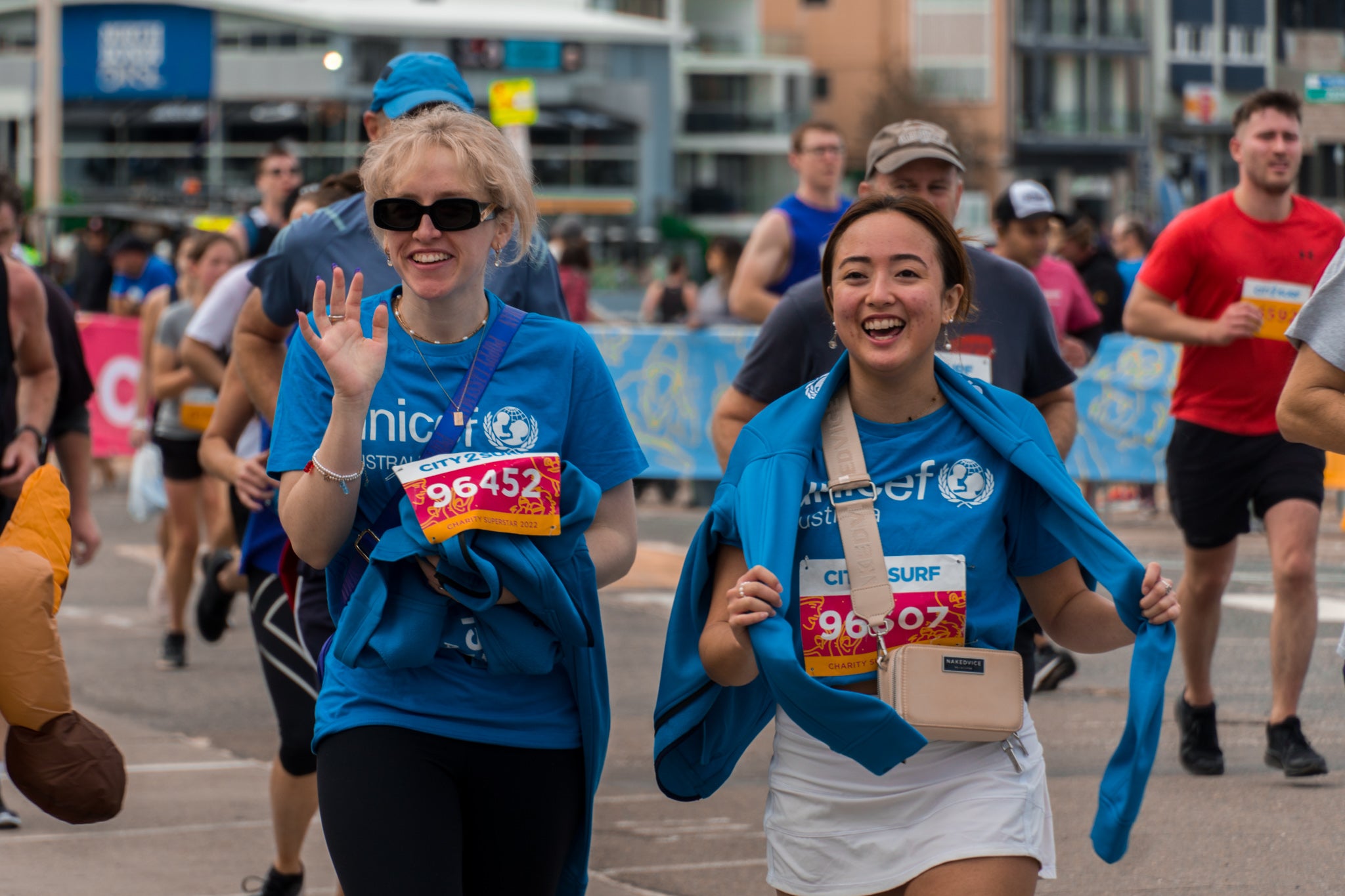 Two women wearing UNICEF T-shirts smile and wave.