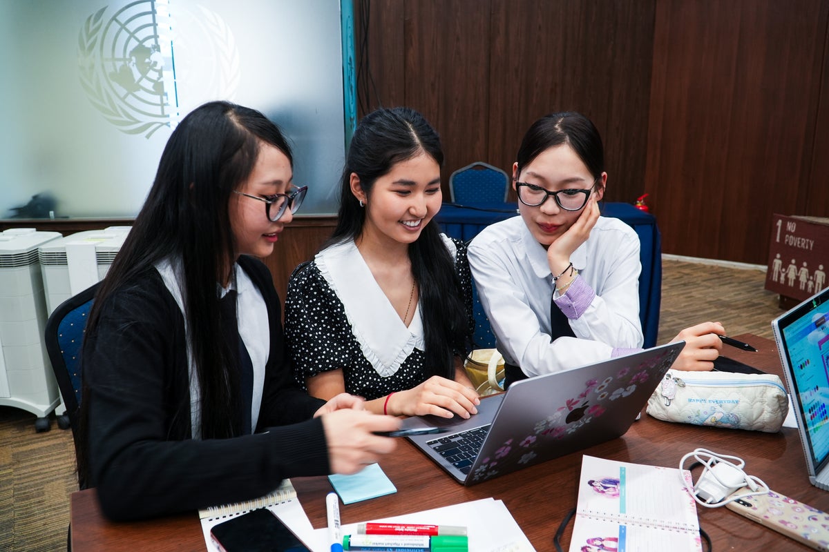A girl on a laptop working with two of her teammates.