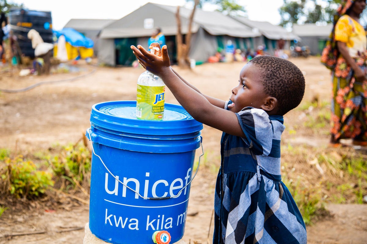 A young girl washes her hands with a UNICEF bucket in an emergency camp in Tanzania.  