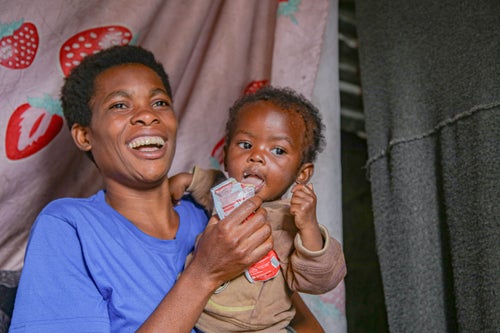 A mother holds her child who has Plumpy 'Nut Peanut Butter in her hand