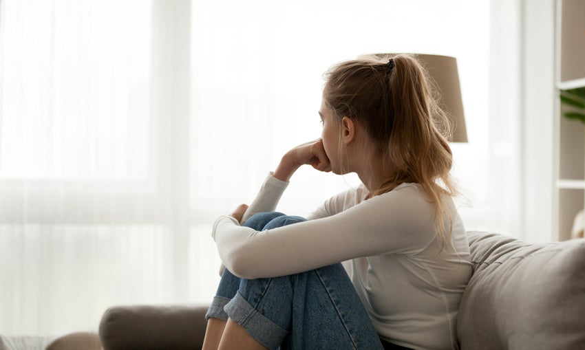 A teenage girl leaning her head on her hand looks out thoughtfully into the distance.