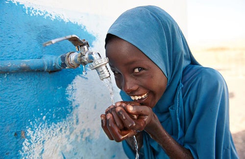 A girl drinking water from a tap.